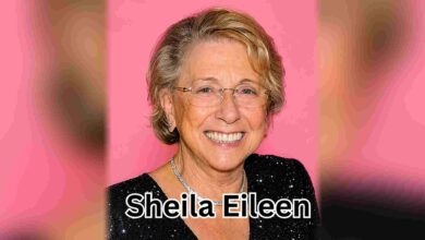 A color portrait of older Sheila Eileen smiling in a black sequined dress against a pink background.