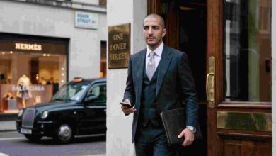 A candid photograph of Qatari businessman Wissam Al Mana in a grey three-piece suit walking out of the One Dover Street building in London. A Hermès store is visible in the background.